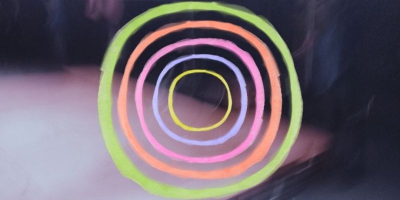 Mehrere handgezeichnete, ineinanderliegende Kreise in Neonfarben auf dunklem Hintergrund.